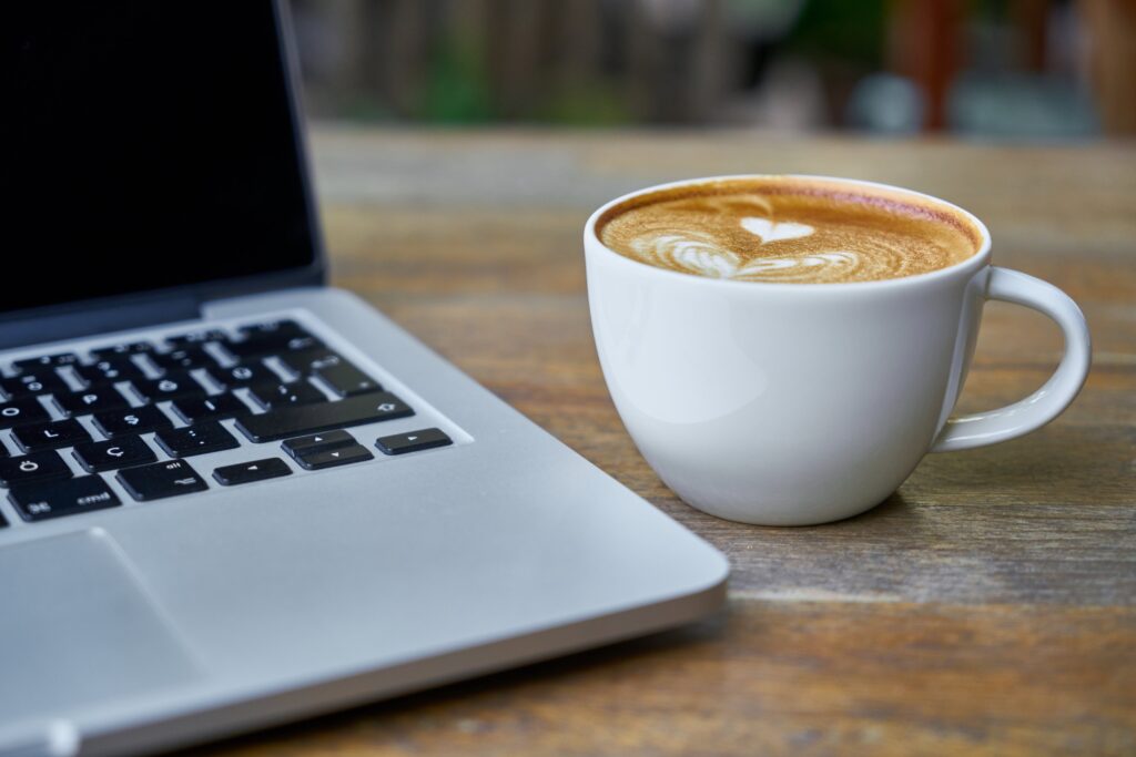Terveysdata-aamukahvit. Kahvi vaahdotetulla maidolla valkoisessa kupissa kannettavan tietokoneen vierellä.